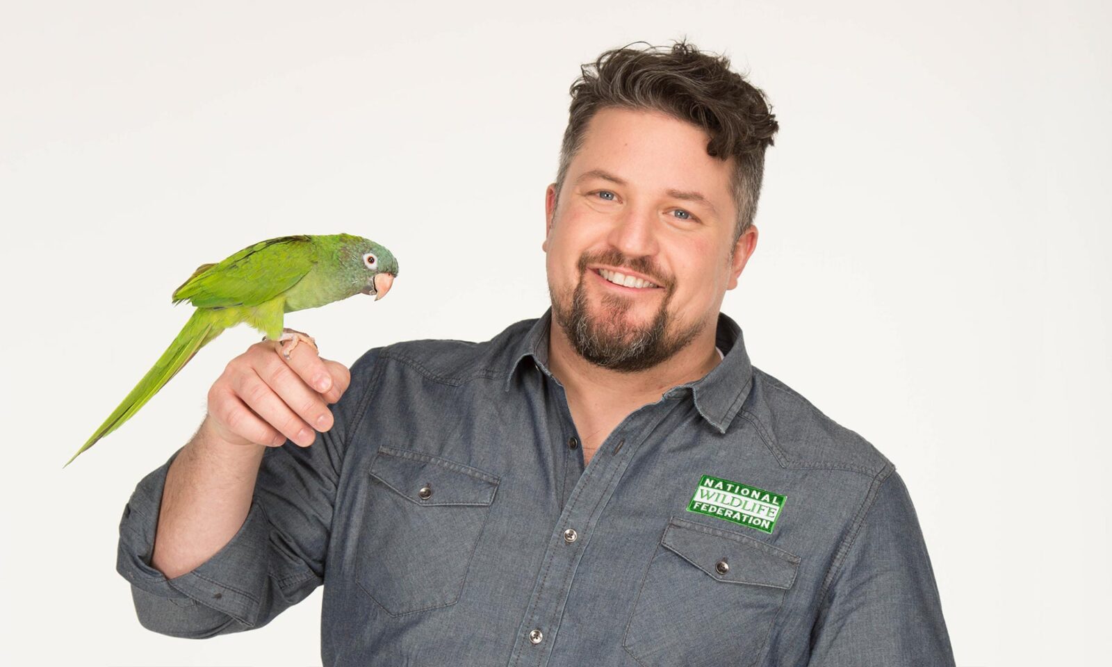 David Mizejewski holds a green parrot on a finger and smiles at the camera
