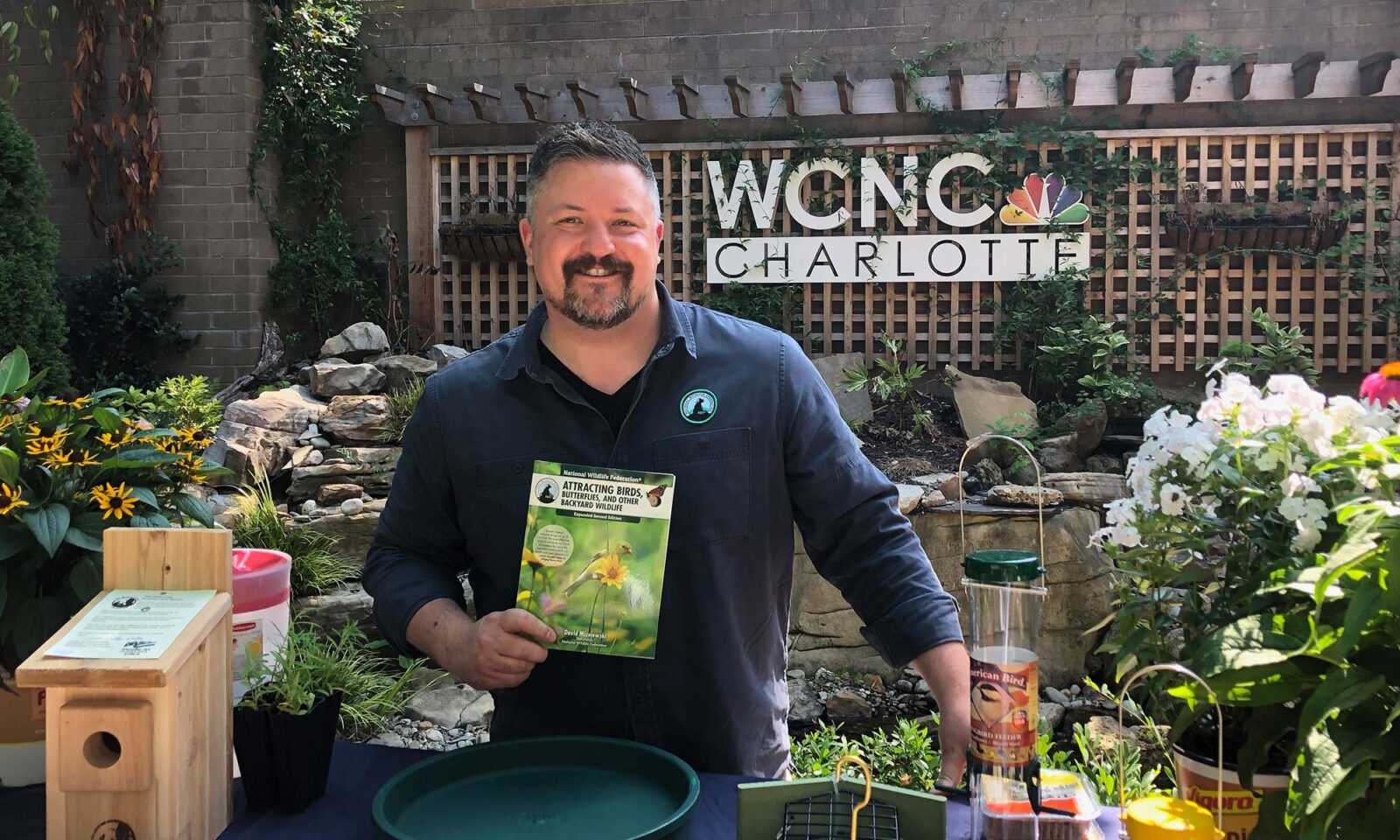 David Mizejewski stands in a garden and holds up his book, "Attracting Birds, Butterflies, and other Backyard Wildlife"